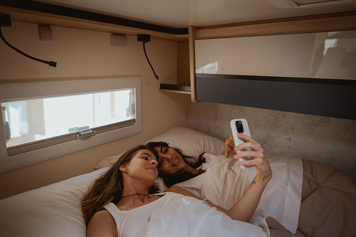 Due persone rilassate nel letto di un camper, sfogliano le card di Girablog su un camper CI Honor.